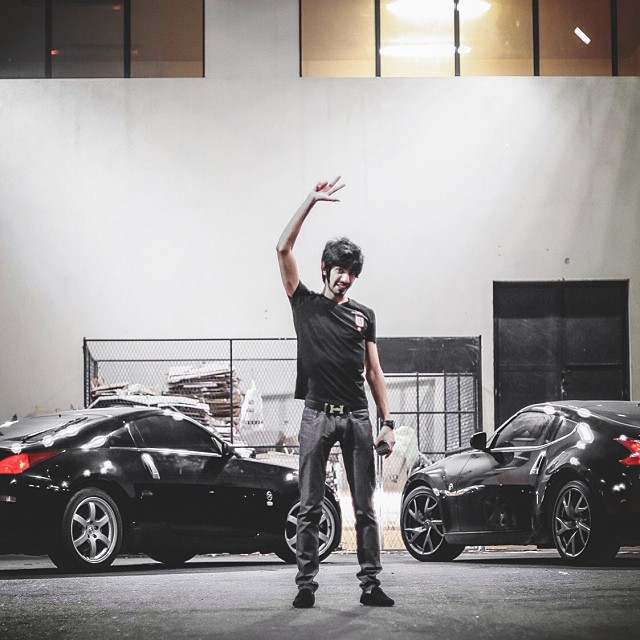 a man wearing a black shirt standing in front of three sports cars