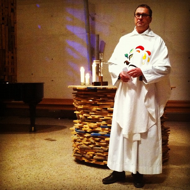 priest stands before lit candles and basket in church