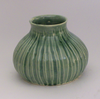 a green vase is shown on a white table
