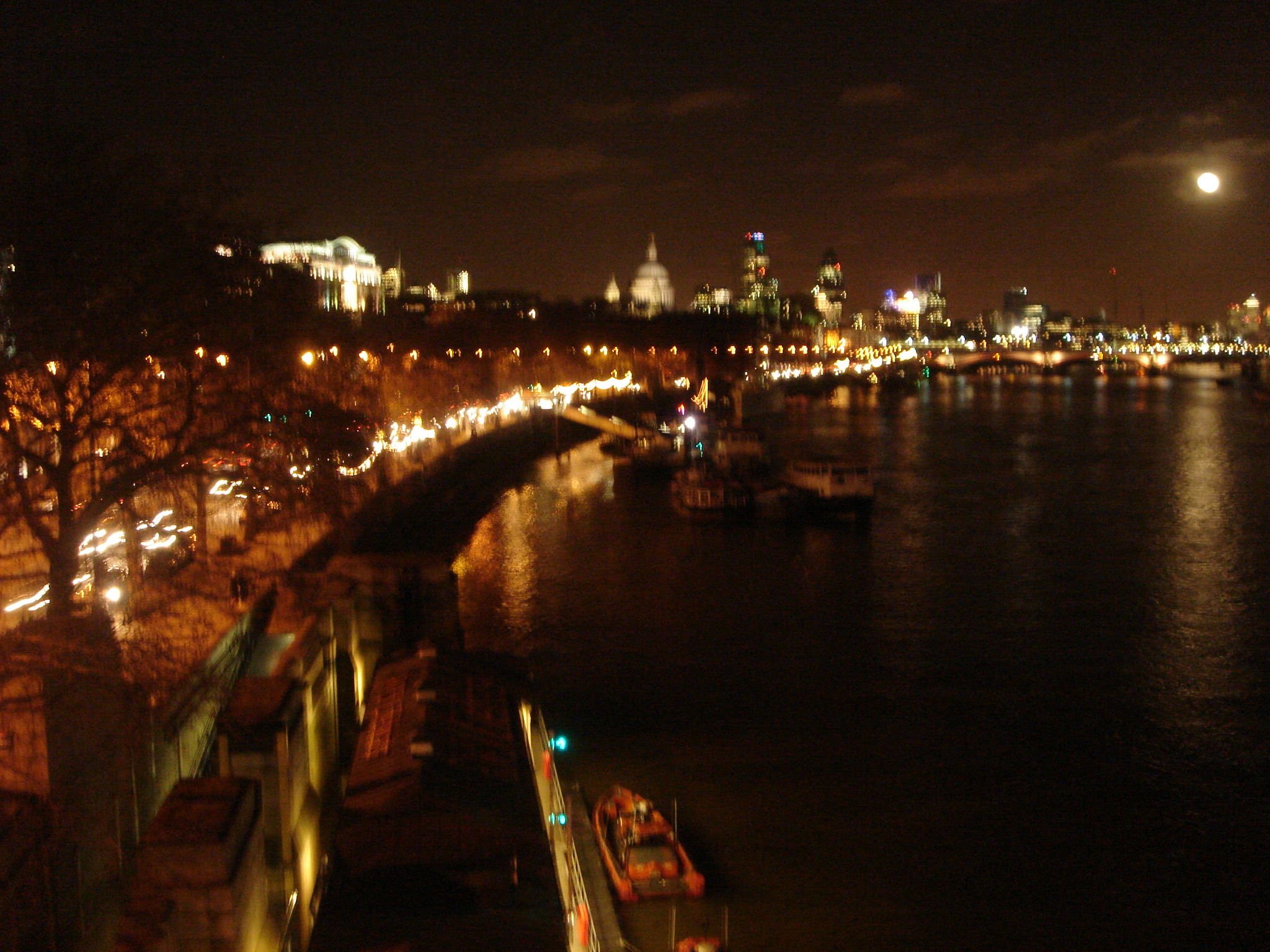 a night time view of boats on the water near the city lights