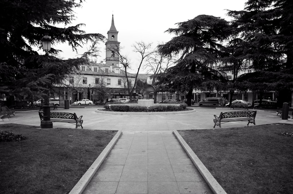 a black and white image of a street, a church and a fountain
