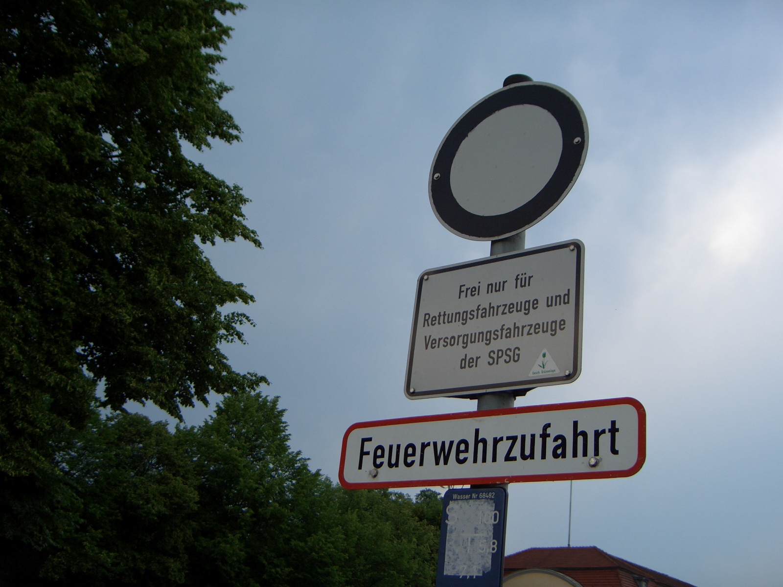 a street sign in german with a clock and some trees in the background