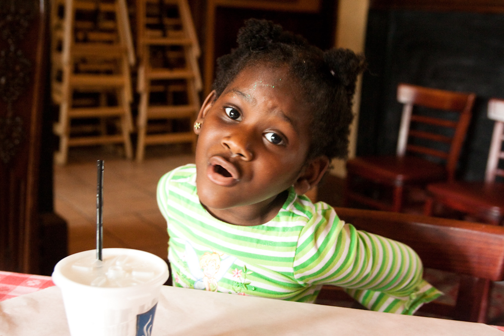 a little girl sitting at a table with a plastic cup on her lap