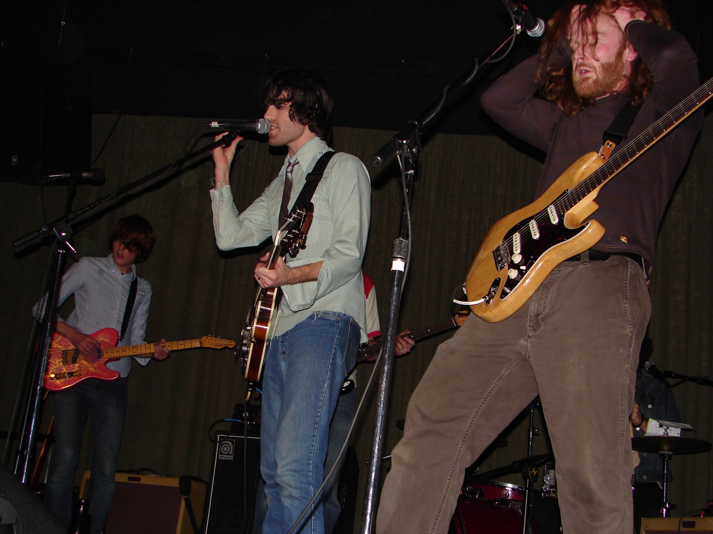 one man on stage and the other singing while another man plays on guitar