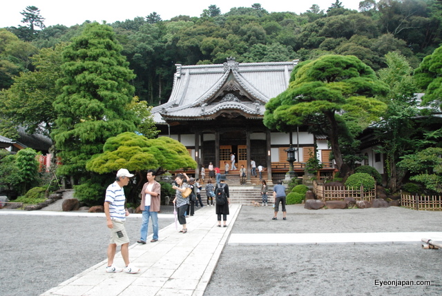 people walking through a park near a large oriental house