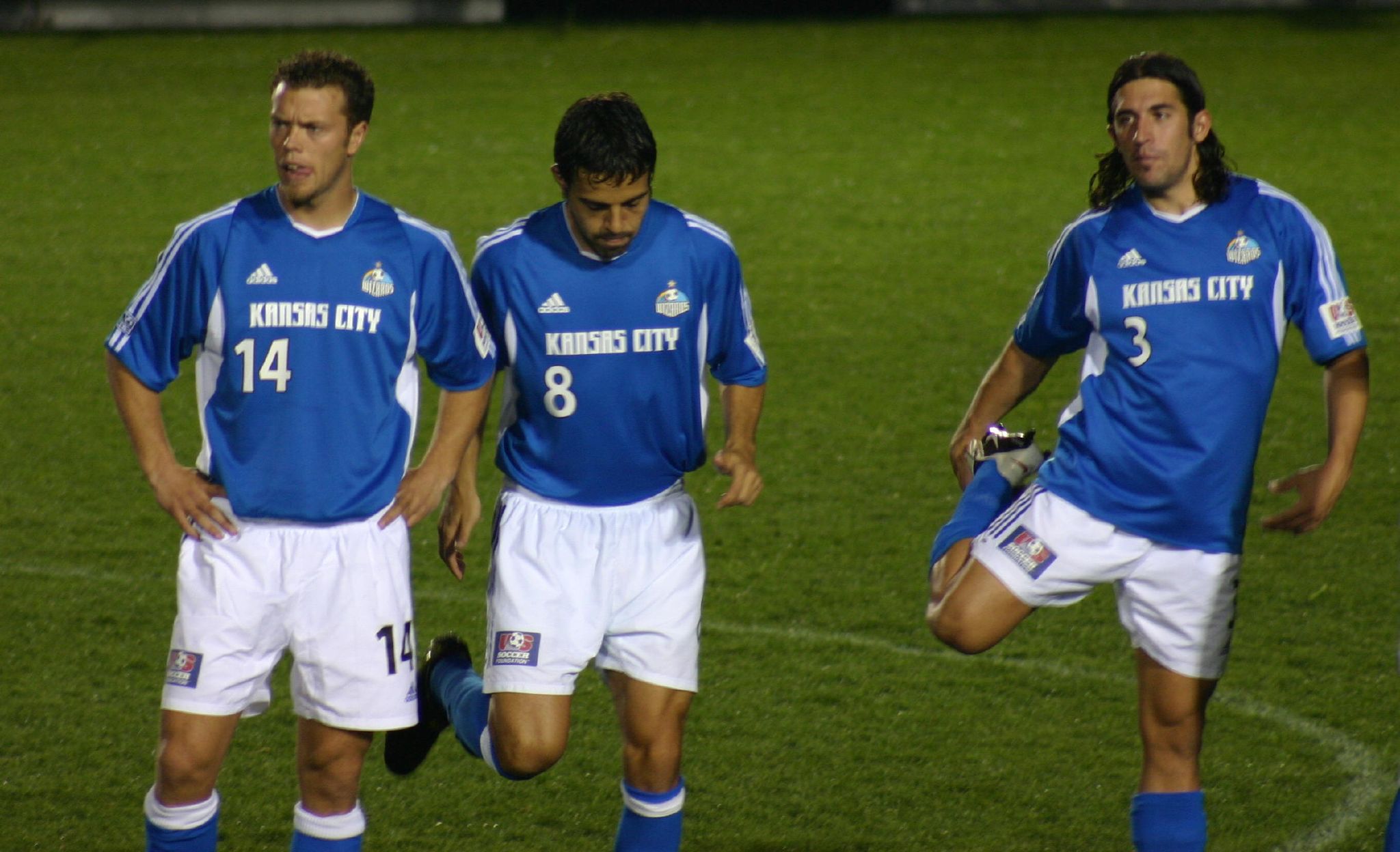 three soccer players with knee pads and shorts walking on the field