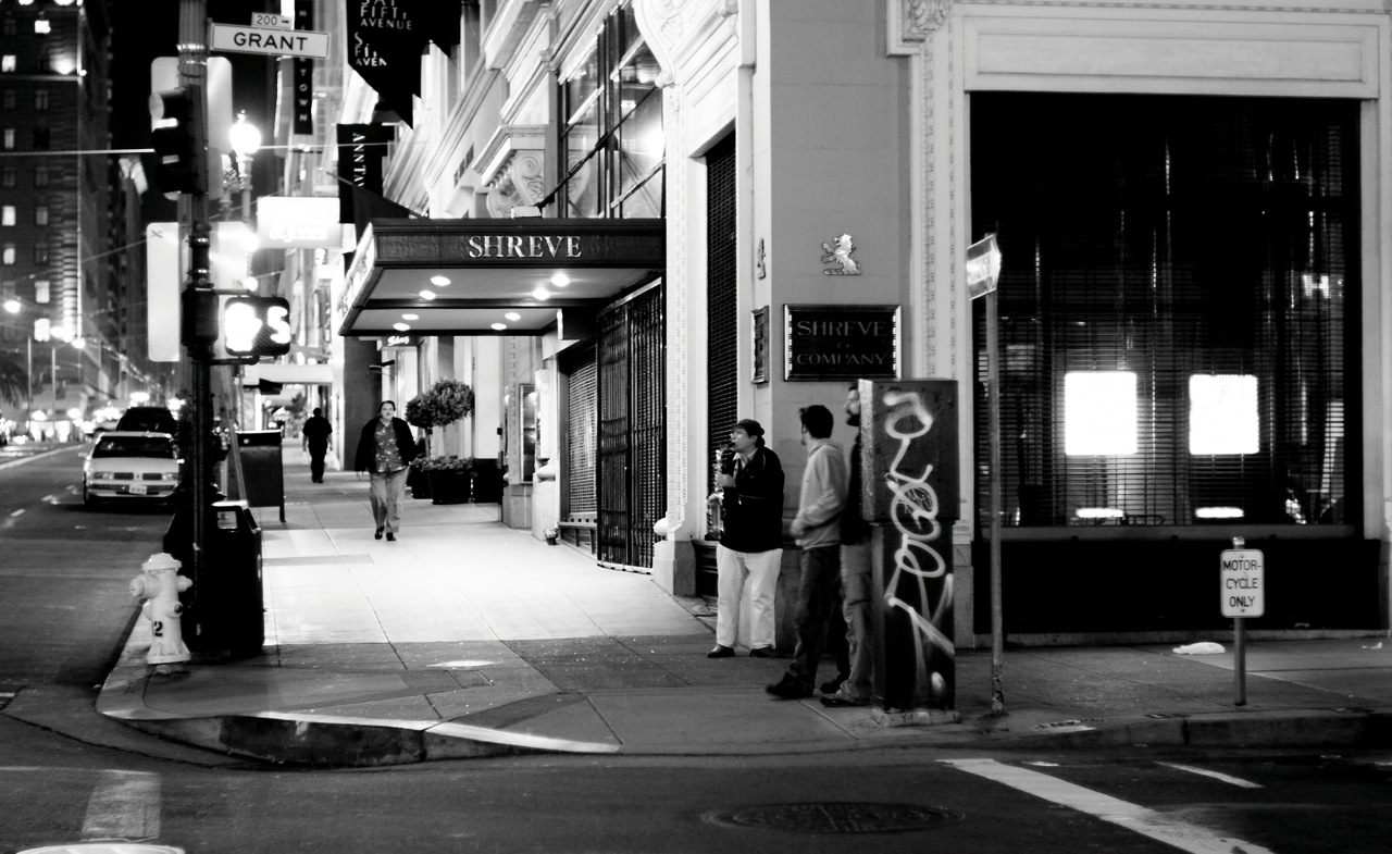 people are standing on a sidewalk waiting for their bus