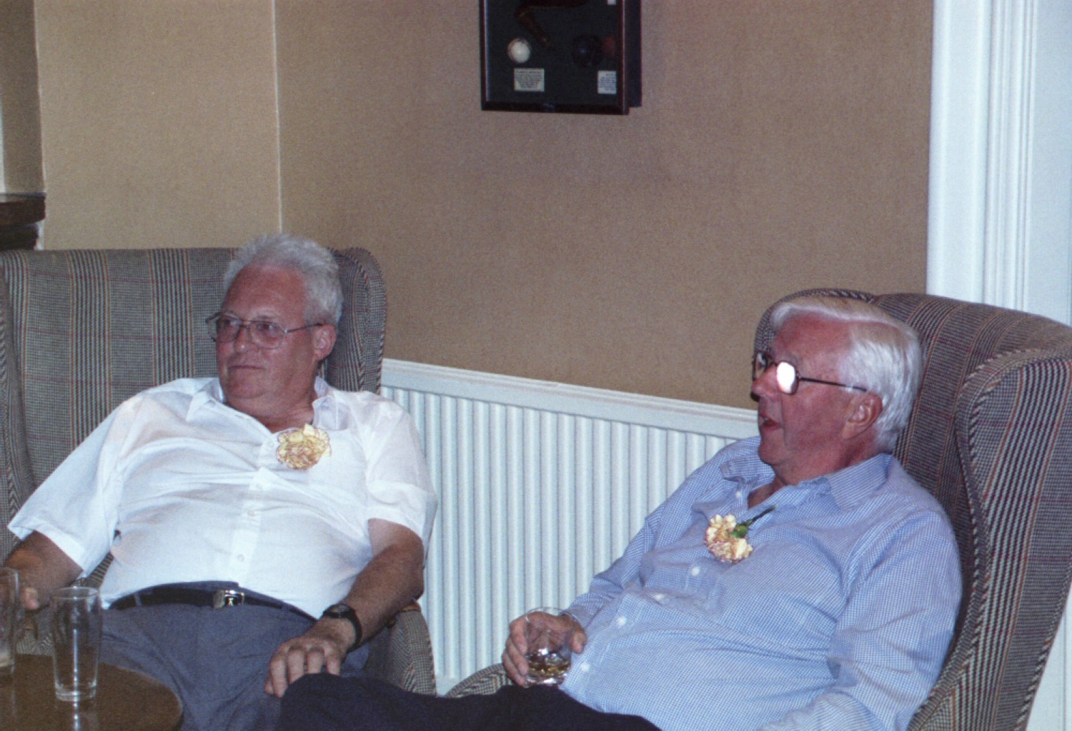 a couple of men sitting down and one is wearing a flower