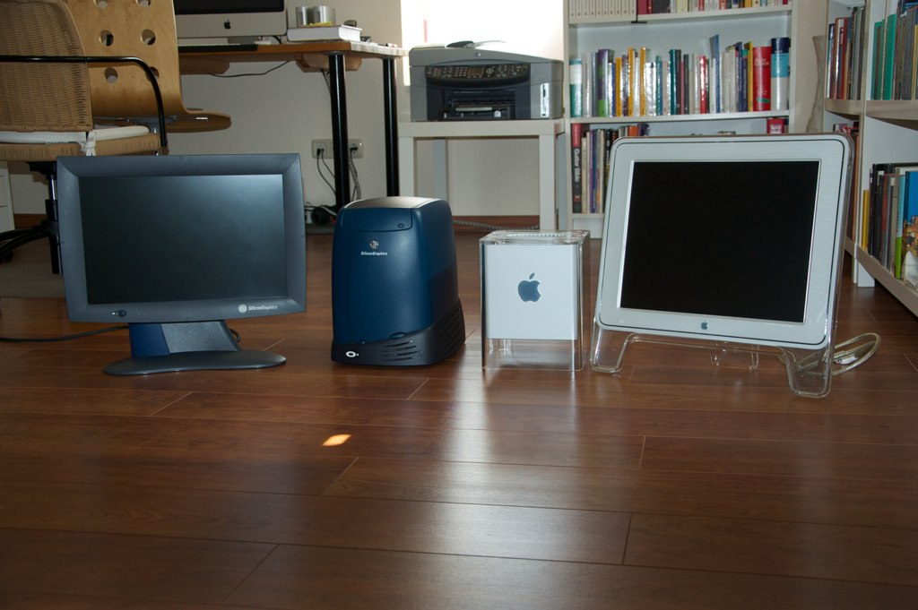 three computers in front of several bookshelves with a desk top