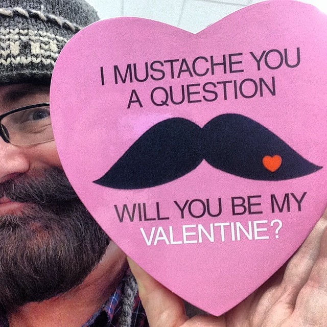 a man holding a pink heart with mustaches and a question