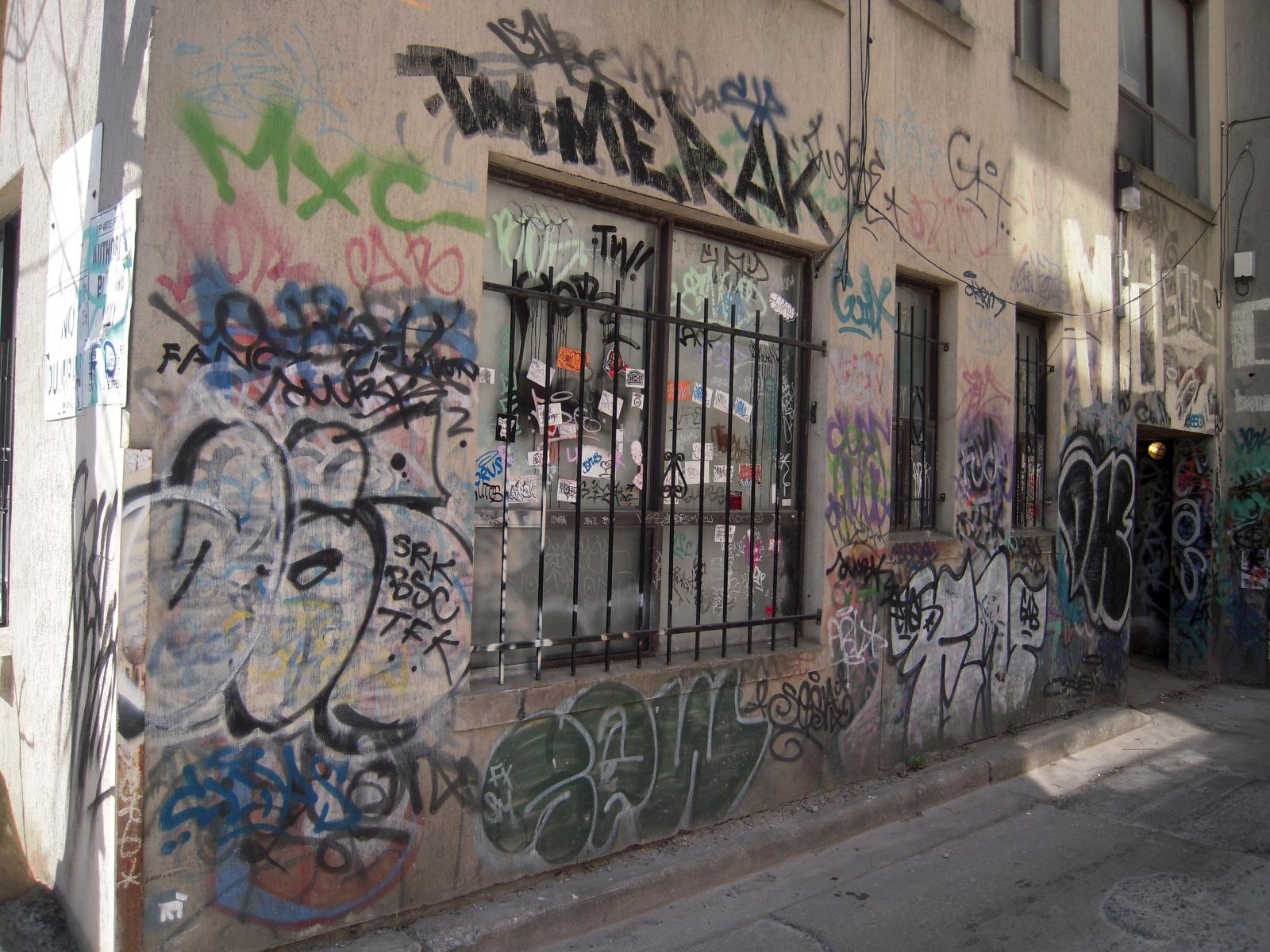 a narrow city street with a building covered in graffiti