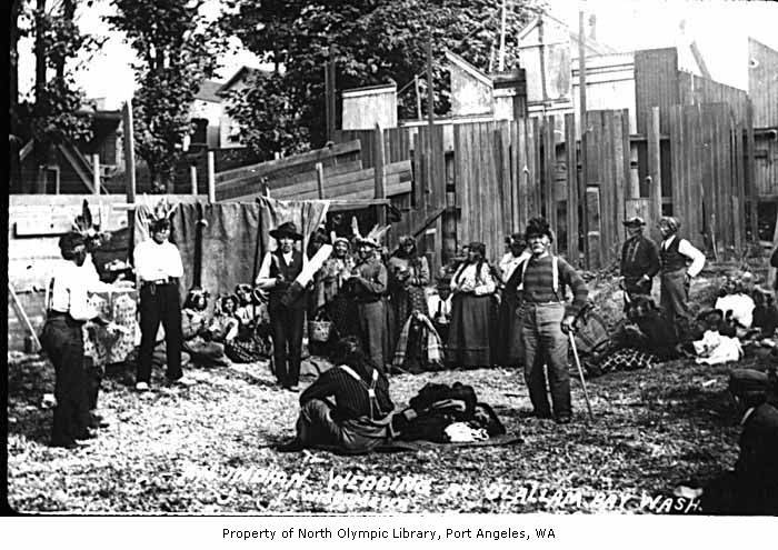old picture of group with various clothing and equipment in the background