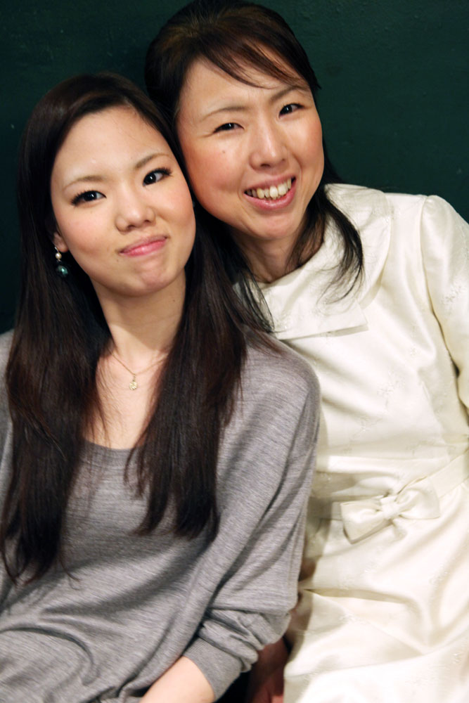 two asian women smiling with one holding her shoulder