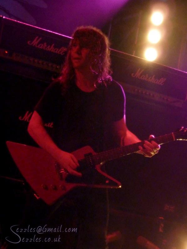 a man with long hair playing guitar in front of purple light
