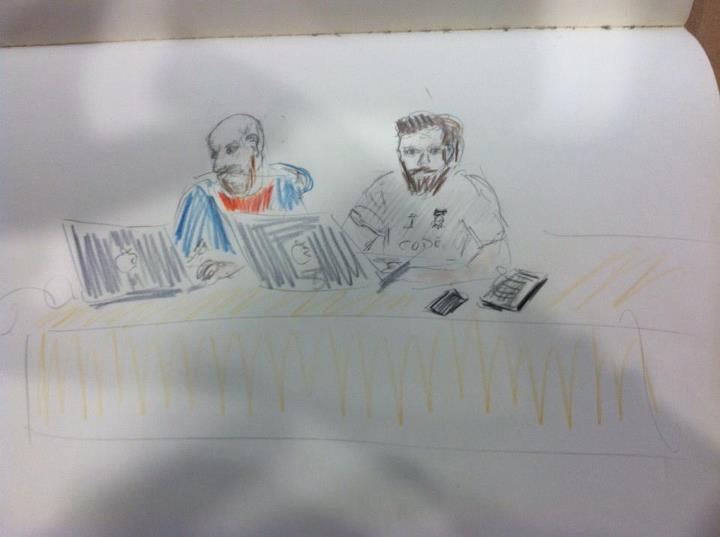 two men sitting at a table with laptops