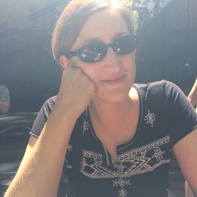 a woman in black shirt and sunglasses laying on top of a bench