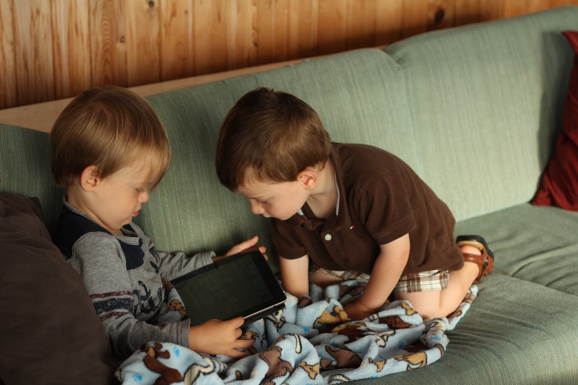 two boys are laying on the couch playing with an electronic device