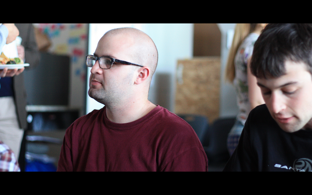 a man wearing glasses while sitting next to another man