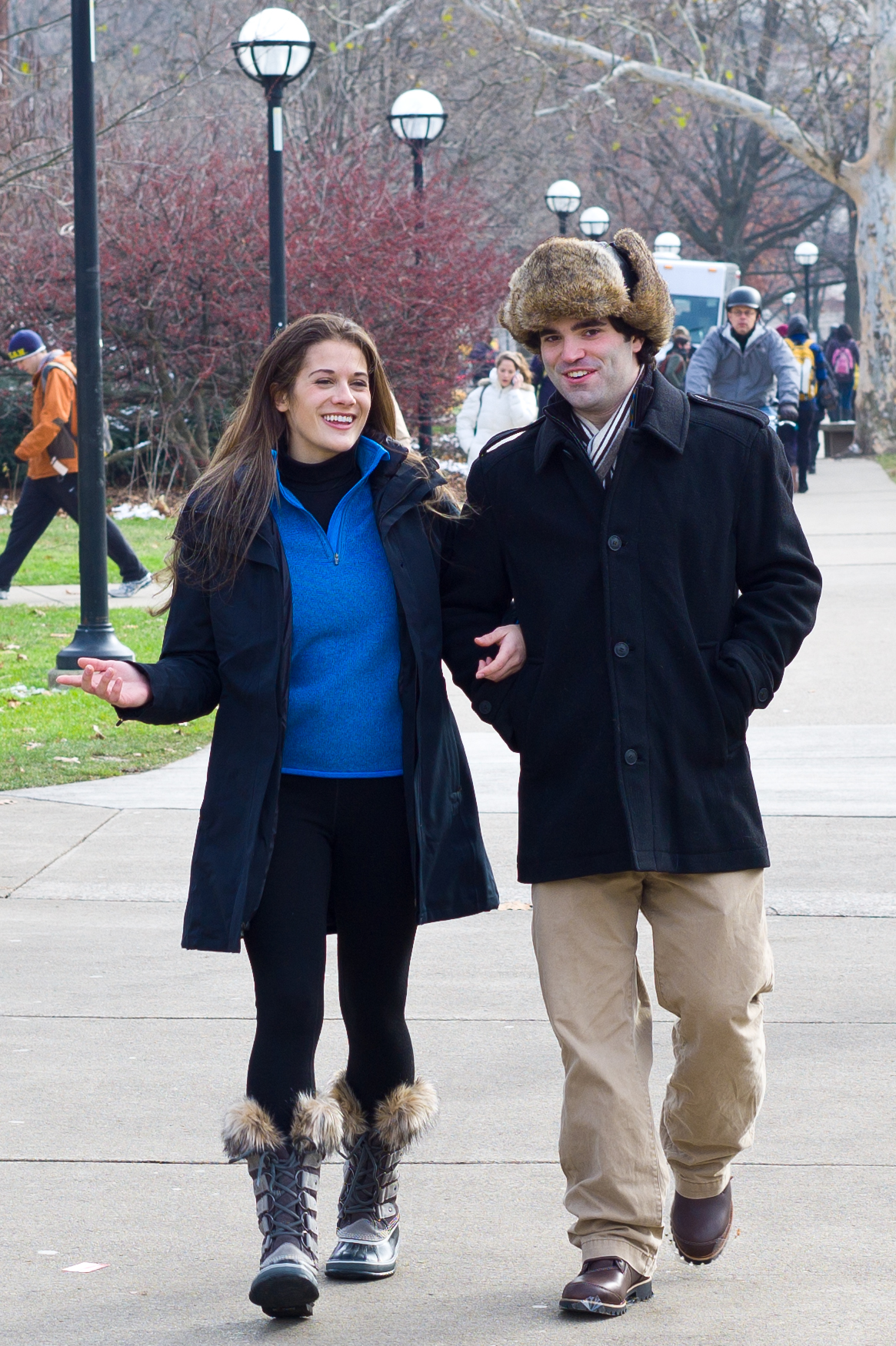 a young man and woman walk down the sidewalk in winter clothing