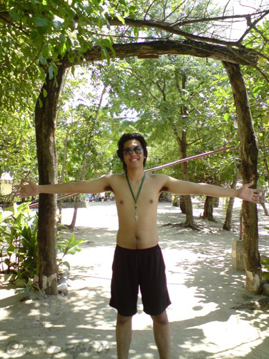 a shirtless man with his arms open in front of trees