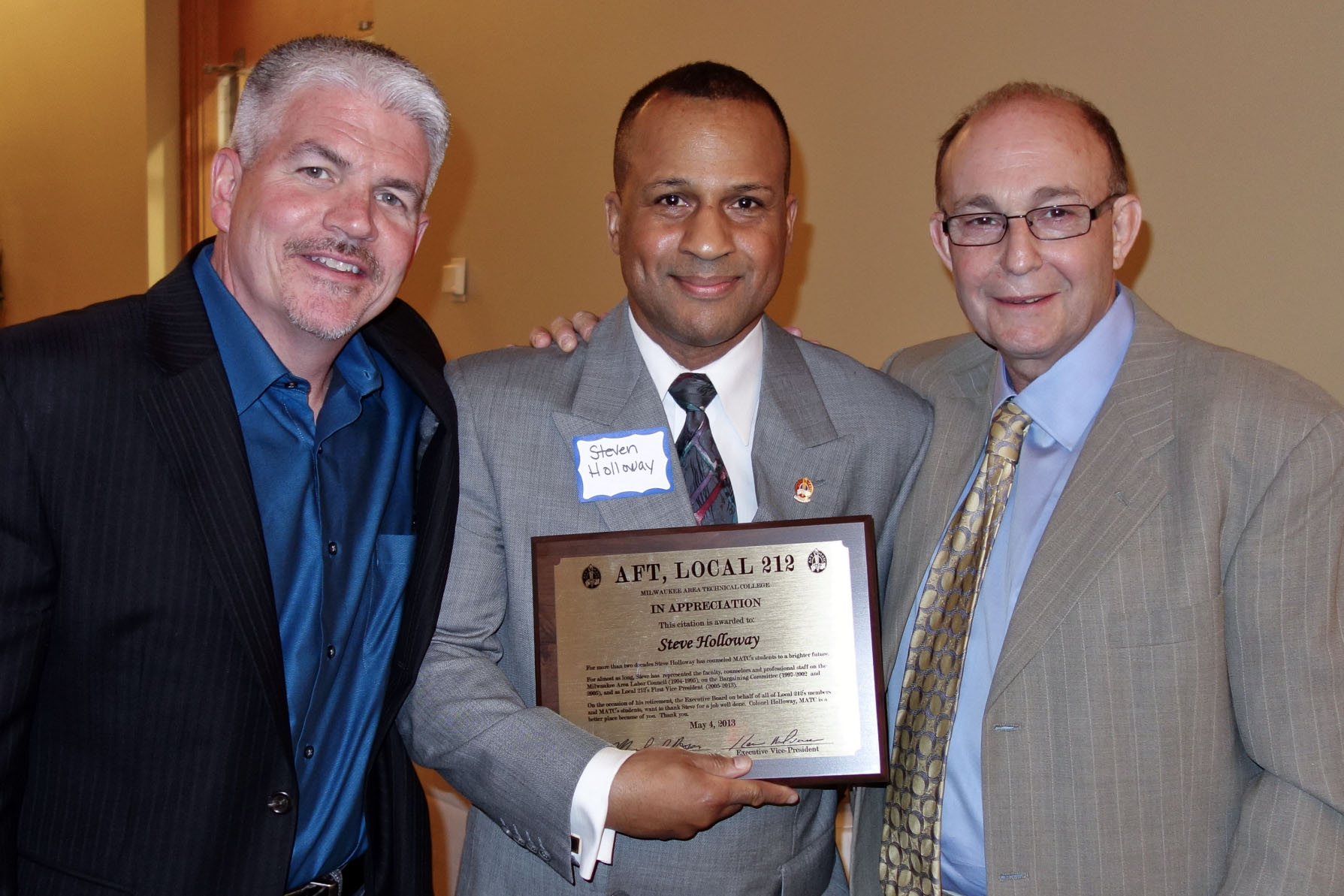 three men are standing side by side, posing with a plaque