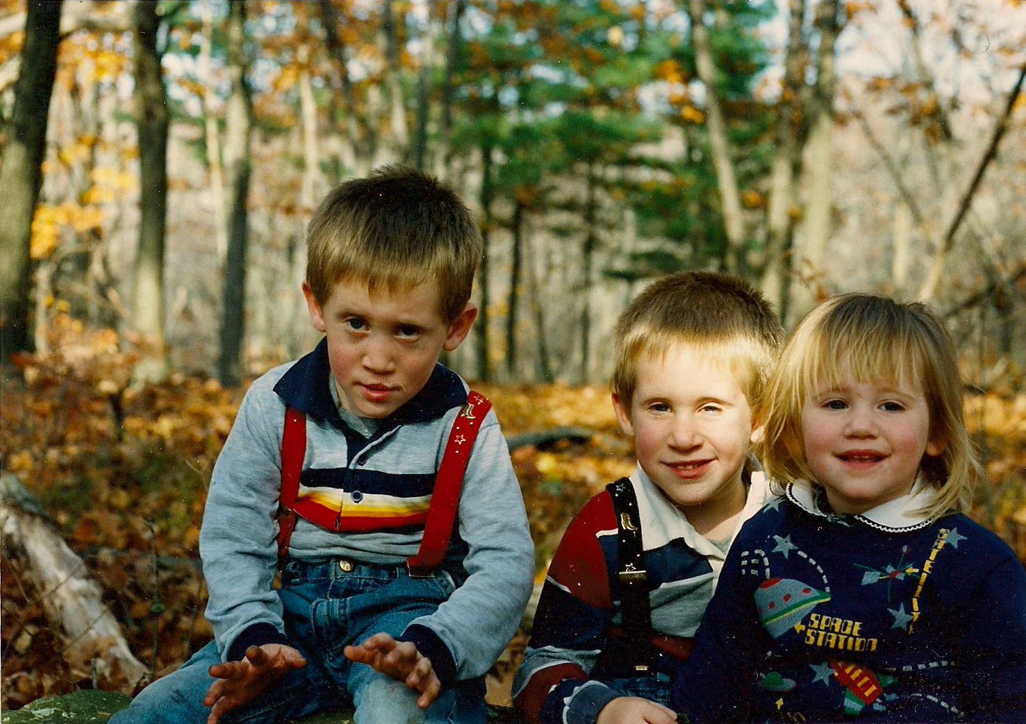 three small boys sitting on a piece of wood