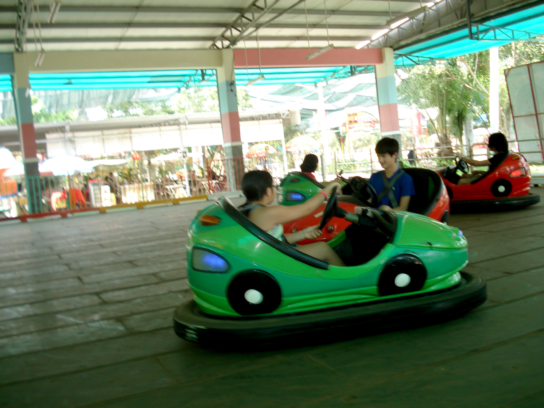people in bumper cars at a park with others watching