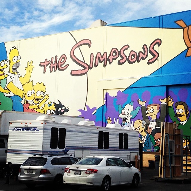 cars are parked near a wall with simpsons's on it