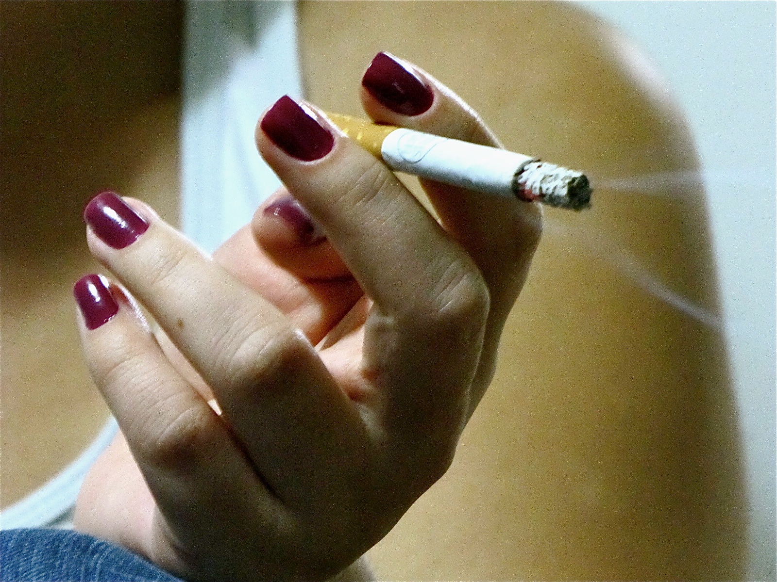 a woman with red and white nail polish holding a cigarette in one hand