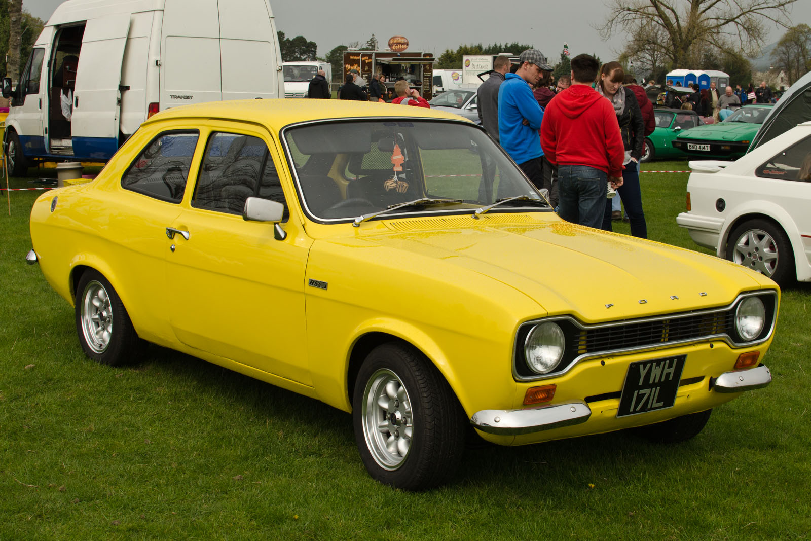 an old yellow car on some grass near other vehicles