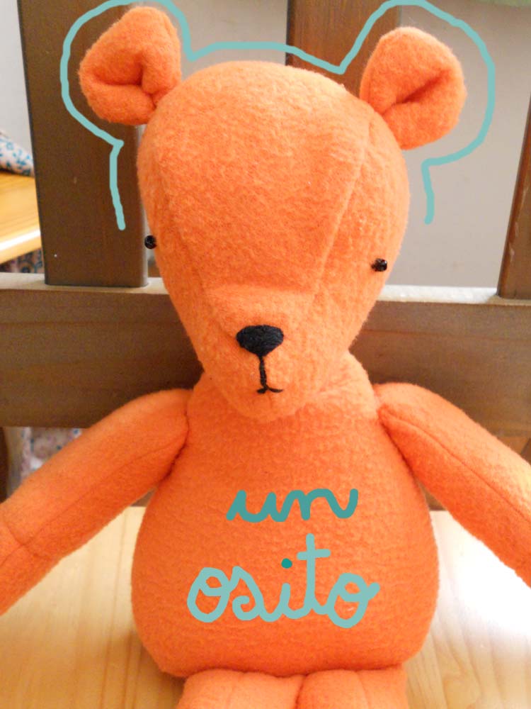 a bright orange stuffed bear is posed on the table
