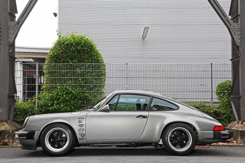 a silver porsche parked near a fence in front of a house