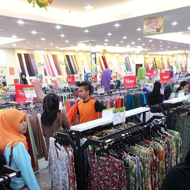 there is a man and woman standing at the rack of scarves