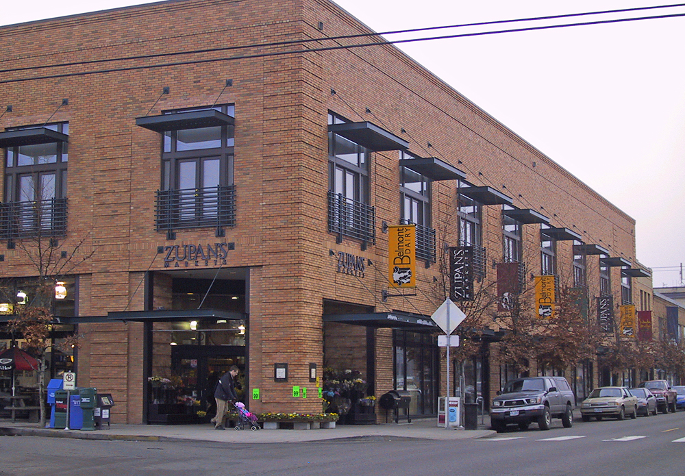 an intersection in front of a brick building with cars parked in front