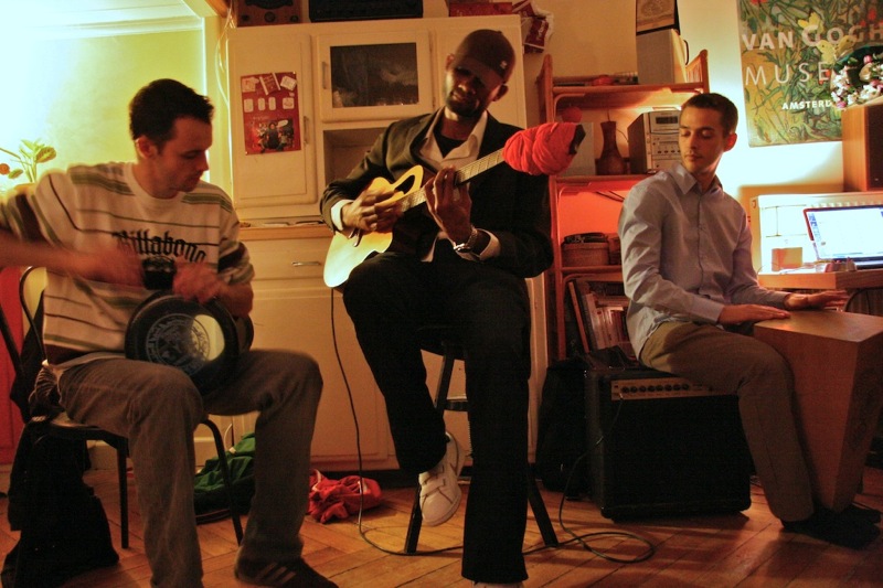 three men playing instruments in an apartment kitchen