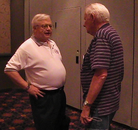 an older man in a blue and white striped shirt standing near another man in jeans