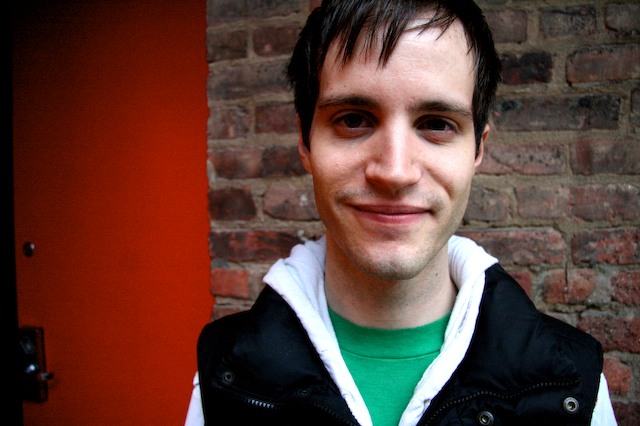 a man in a vest and a green shirt smiles at the camera