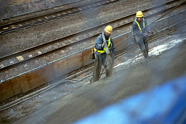 some men wearing helmets and work clothes next to railroad tracks