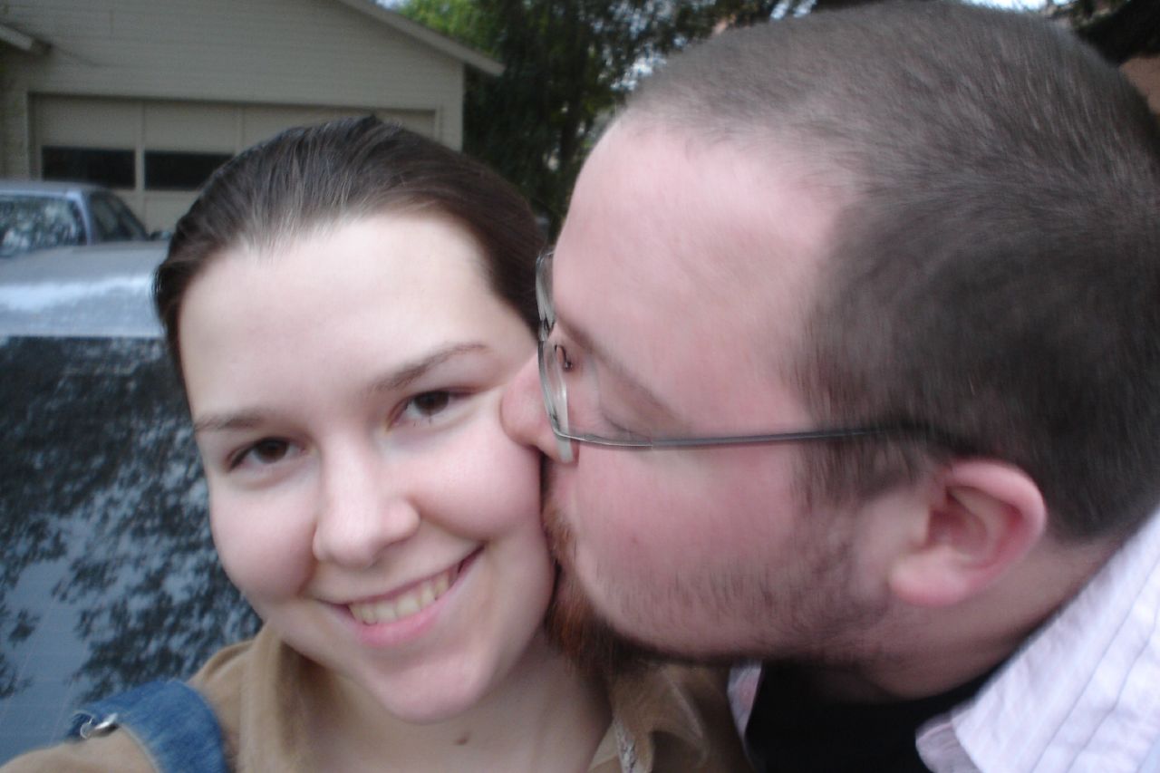 a couple kissing and smiling next to a house