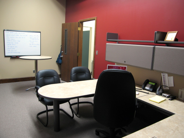 the room has an office desk and two chairs, which are in front of the projector screen