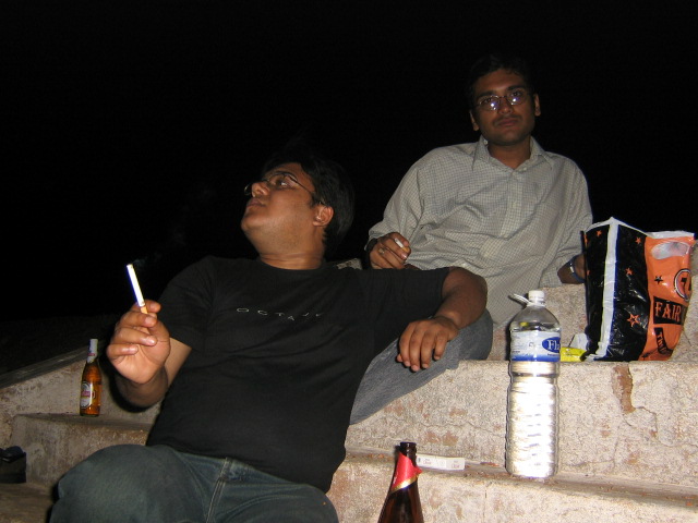 two men sit on the edge of a building next to a beer bottle