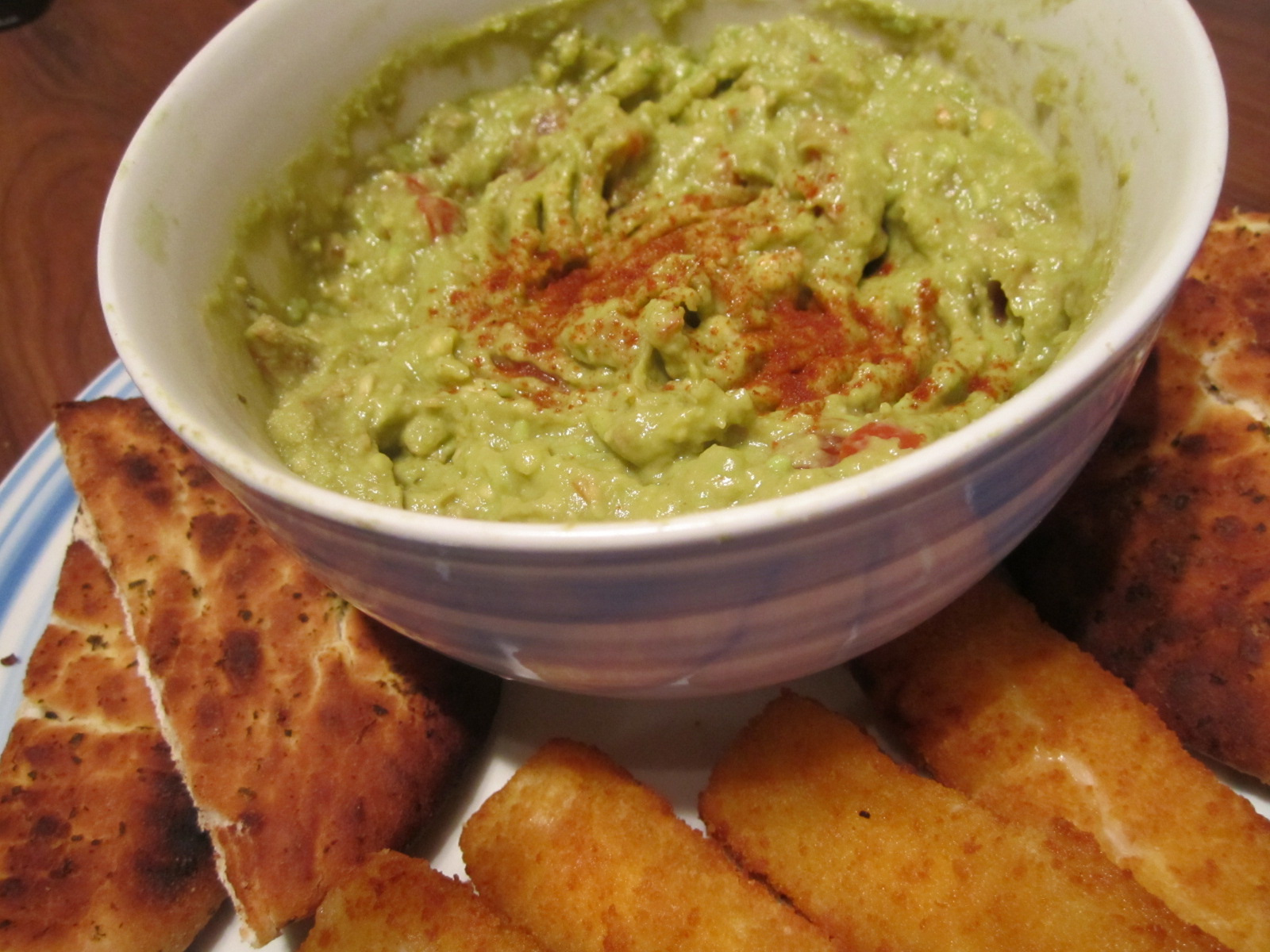 a white plate with some breadsticks and guacamole in it