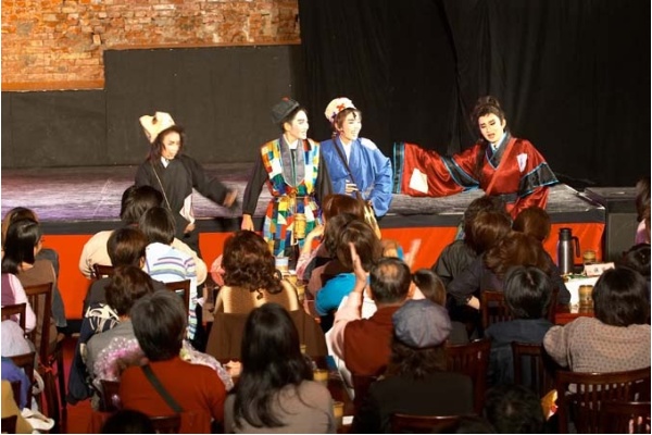 men in asian clothing perform on stage to an audience