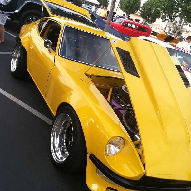 a yellow sports car sits on a street with people nearby