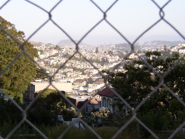 the view is behind a wire fence, looking down at a suburban neighborhood