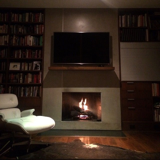 a television above a fireplace with many books