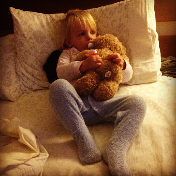 a small child sitting on a bed with a teddy bear