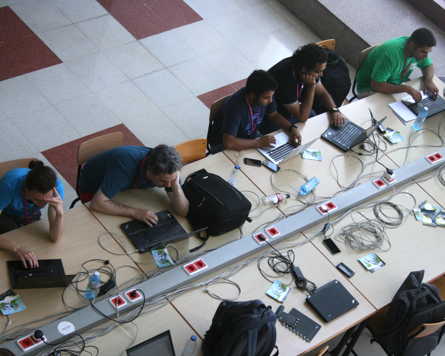 a group of men on laptops and wires, sitting at a table