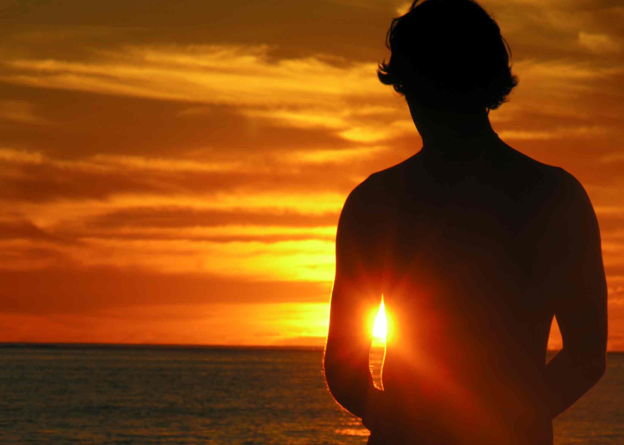 silhouette of person standing at ocean on sunset