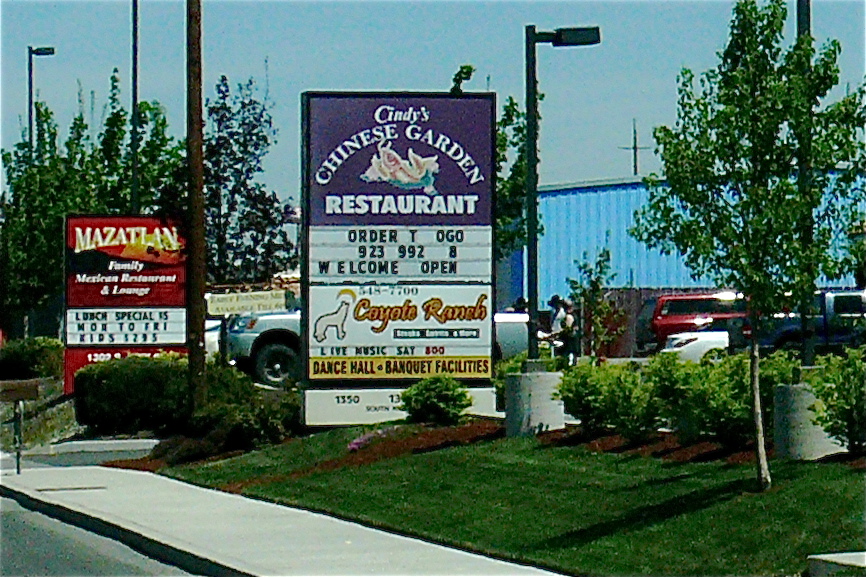a restaurant sign sitting in the grass on the side of the road